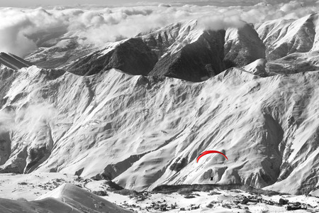 Black and white view on paragliding at snowy mountains over ski resort and off-piste slope at sunny winter evening. Caucasus Mountains. Georgia, region Gudauri. Selective color effect.の写真素材