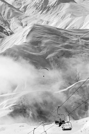 Chair-lift and paraplane in fog on ski resort at cold winter day. Snowy Caucasus Mountains. Georgia, region Gudauri. Black and white toned landscape.の写真素材
