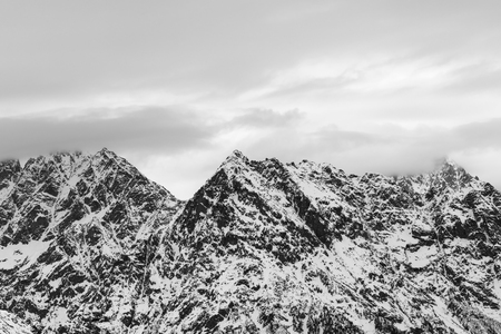 Rocky mountains in snow and cloudy gray sky at winter. Caucasus Mountains, Svaneti region of Georgia. Black and white toned landscape.の写真素材