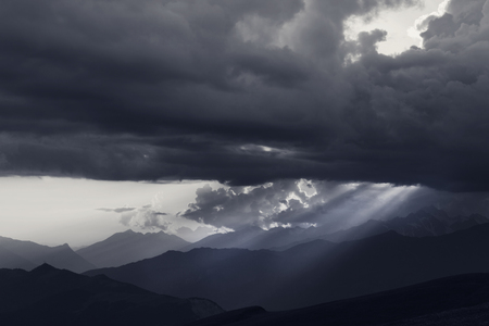 Silhouettes of cloudy mountains and sunbeams at summer evening. Caucasus Mountains. Georgia, region Svaneti. Black and white toned landscape.の写真素材