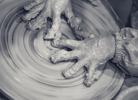 Hands of young girl in clay on pottery wheel. Potter at work. Close-up view. Black and white toned image.の写真素材