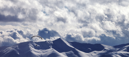 Panoramic view on evening sunlight mountain with clouds and silhouette of paraglider. Snowy Caucasus Mountains at winter. Georgia, region Gudauri.の写真素材