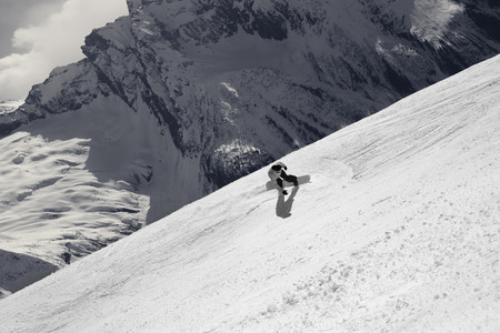 Snowboarder descends on off-piste ski slope in high snowy mountains at sunny winter day. Caucasus Mountains, region Dombay. View from above. Black and white retro toned landscape.の写真素材