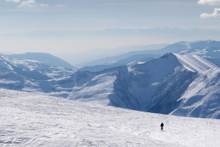 Silhouette of skier on snowy off-piste slope and mountains in haze at sunny winter morning. Caucasus Mountains, Georgia, region Gudauri.の写真素材
