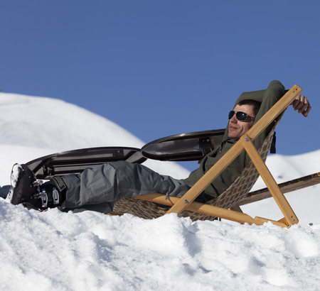 Skier at winter snowy mountains resting on sun-lounger at sunny day. Caucasus Mountains, Georgia, region Gudauri.