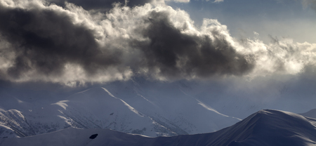 Panoramic view on snowy evening mountain and sunlit clouds. Caucasus Mountains, Georgia, region Gudauri in winter.の写真素材
