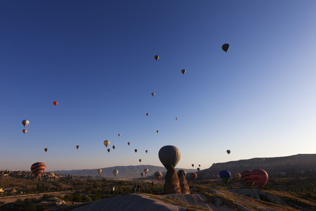 GOREME, CAPPADOCIA, TURKEY - MAY, 2013: Lot of multicolor hot air balloons on blue clear sunlit sky and fairy chimneys rock formations at sunrise. Wide-angle view.のeditorial素材