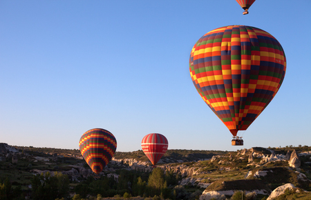 GOREME, CAPPADOCIA, TURKEY - MAY, 2013: Multicolor hot air balloons on clear sunlit sky and rocks with grass at sunny spring morningのeditorial素材