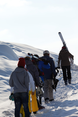 Skiers and snowboarders with skis and snowboards go up on snowy road at sun winter morning. Caucasus Mountains, Georgia, region Gudauri.の写真素材