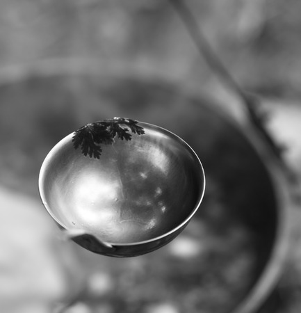 Black and white metal ladle (spoon) and soup in cauldron at background. Outdoor camping cooking. Selective focus.の写真素材