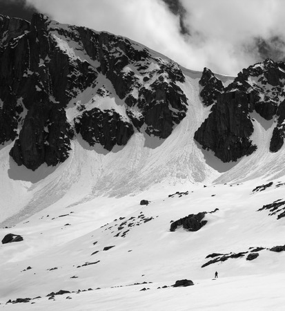 High mountains with snow cornice and avalanche tracks, snowy plateau and small silhouette of hiker at sunny day. Turkey, Kachkar Mountains, highest part of Pontic Mountains. Black and white toned landscape.の写真素材