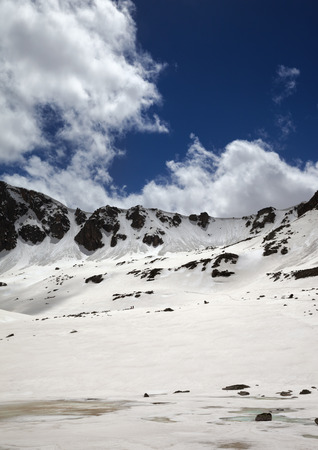 Frozen lake covered with snow, sunlit mountain pass and blue cloudy sky at spring. Turkey, Kachkar Mountains, highest part of Pontic Mountains.の写真素材