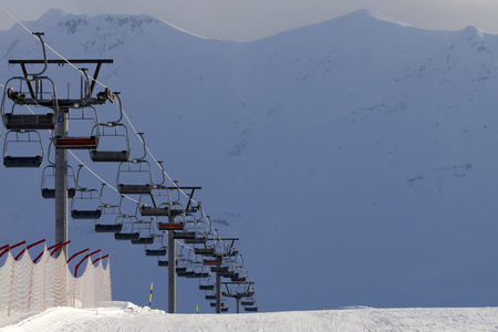 Snowy ski slope and chair lift on high mountains at winter evening. Caucasus Mountains. Georgia, region Gudauri.の写真素材