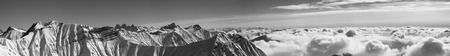 Large panorama of snowy mountains covered with beautiful sunlight clouds at sunny winter day. Caucasus Mountains, Georgia, region Gudauri. Black and white toned landscape.の写真素材