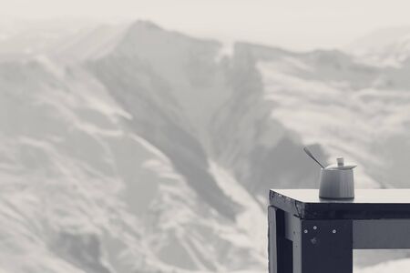 Old table with sugar bowl in outdoor cafe at ski resort and snowy sunlight mountains at background. Black and white retro toned landscape.の写真素材
