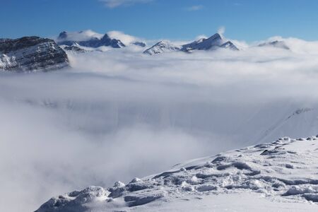 Snowy slope and sunlit mountains under clouds at nice sun day. Caucasus Mountains in winter, Georgia, region Gudauri. Viewpoint atop mount Kudebi.の写真素材