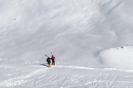 Two skiers with skis on his shoulder and snowy off-piste slope with traces of skis and snowboards. Caucasus Mountains in sun cold winter day, Georgia, region Gudauri.の写真素材