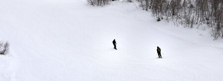 Panoramic view on skier and snowboarder on snowy ski slope at gray winter dayの写真素材