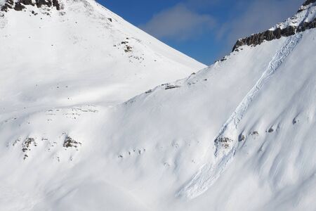 Snowy off-piste slope with traces of skis, snowboards and avalanches. Caucasus Mountains in sunny winter day, Georgia, region Gudauri.の写真素材