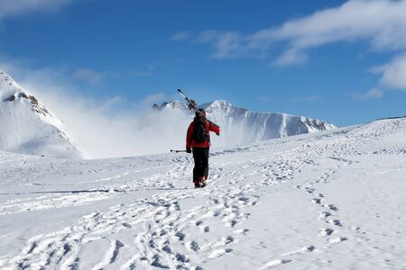 Skier with skis on his shoulder go up to top of snowy mountain in nice sun day. Caucasus Mountains in winter, Georgia, region Gudauri, Mount Kudebi.の写真素材