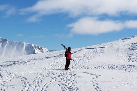 Skier with skis on his shoulder and snowy mountain in cold sunny day. Winter Caucasus Mountains, Georgia, region Gudauri, Mount Kudebi.の写真素材