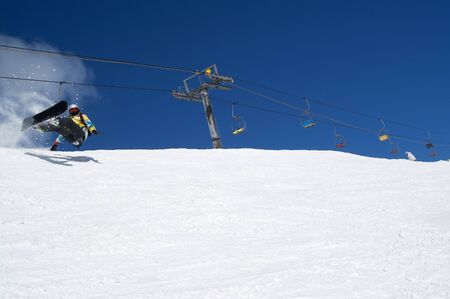 Snowboarder fall down with snow splashes on snowy ski slope and chair lift at background. Caucasus Mountains in sunny winter day, region Dombay.の写真素材