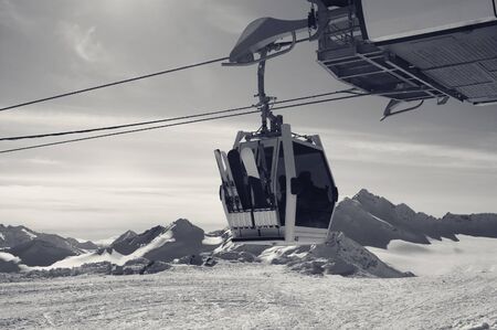 Gondola ski-lift in snowy winter mountains at evening. Caucasus Mountains, mount Elbrus. Black and white retro toned landscape.の写真素材