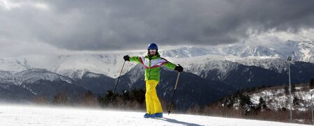 Happy young skier with ski poles in sun mountains and cloudy gray sky before blizzard. Snowy Caucasus Mountains at winter. Hatsvali, Svaneti region of Georgia. Panoramic view.の写真素材