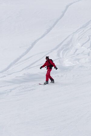Snowboarder in red downhill on snowy off-piste slope after snowfall at gray winter dayの写真素材