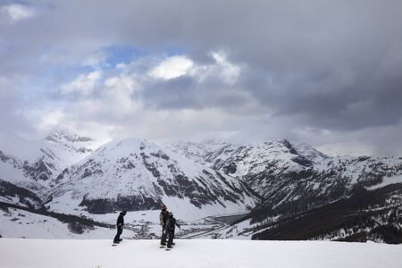 Group of snowboarders starts on off-piste descent. High snowy mountains and cloudy storm sky at winter before blizzard. Ski area Mottolino Fun Mountain, Italian Alps. Livigno, Lombardy, Italy, Europe.の写真素材