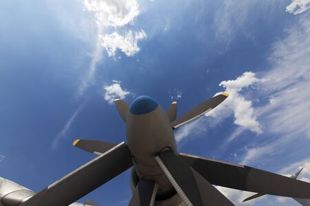 Propeller blade of engine. Part of airplane and sunlit blue sky with clouds at background. Wide-angle view.の写真素材