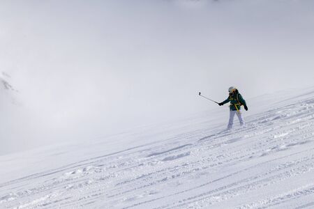 Snowboarder downhill on snowy off-piste slope with newly-fallen snow and high winter mountains in mistの写真素材