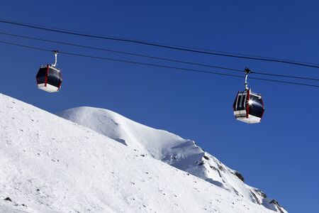 Gondola lift, snowy off-piste ski slope, high winter mountains and blue clear sky in sunny day. Caucasus Mountains. Georgia, region Gudauri.の写真素材