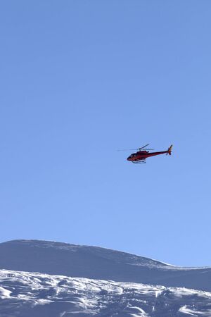 Helicopter in blue clear sky and snowy ski slope in high mountains at sunny winter eveningの写真素材
