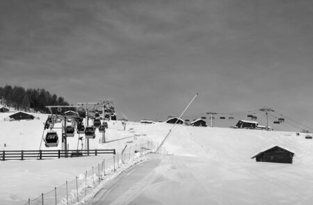 Black and white snowy ski track prepared with snow grooming machine, gondola lift, chair-lift, snow...