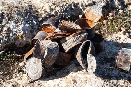 Group of old rusty tin cans covered with ash on stones at sunny day. Concept of environmental pollution, ecological problems.の写真素材