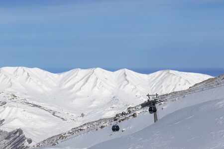 Snowy sunlit mountains and gondola lift at ski resort at sunny winter evening. Caucasus Mountains, Shahdagh, Azerbaijan.の写真素材