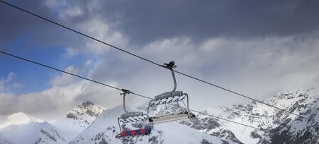 Sunlit chair lift, snowy ski slope, high winter mountains and dark cloudy sky. Ski area Mottolino Fun Mountain, Italian Alps. Livigno, Lombardy, Italy, Europe. Panoramic view.の写真素材