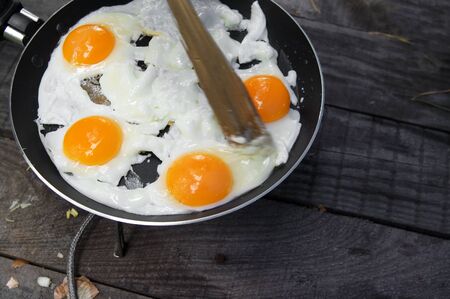 Fried eggs cooked in frying pan on camping gas stove on old wooden table. Outdoor cooking.の写真素材