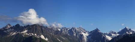Panorama of high rocky mountains with glacier and sunlit blue sky with clouds at summer morning. Caucasus Mountains. Georgia, region Svanetia.の写真素材