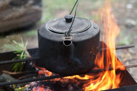 Sooty old teakettle on bonfire with smoke at forest in sunny summer day. Selective focus.の写真素材
