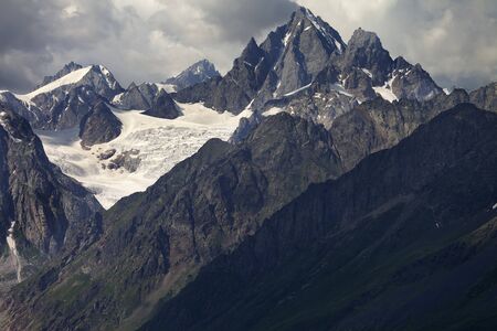 High rocky mountains with glacier in storm clouds before rain. Caucasus Mountains. Georgia, region Svanetia at summer.の写真素材