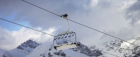 Sunlit chair lift, snowy ski slope, high winter mountains and blue cloudy sky. Ski area Mottolino Fun Mountain, Italian Alps. Livigno, Lombardy, Italy, Europe. Panoramic view.の写真素材