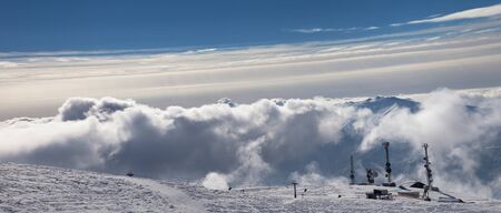 Panoramic view on snowy ski slope, station of ropeway, satellite dishes and roof of hotel in sun cloudy mountains. Caucasus Mountains in winter, Georgia, region Gudauri.の写真素材