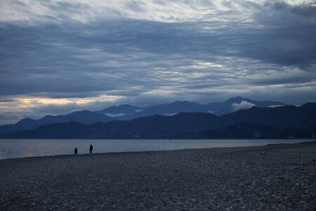 Pebbly beach, sea, silhouette of mountains and cloudy sky at evening. Black Sea coast, Georgia, Batumi.の写真素材