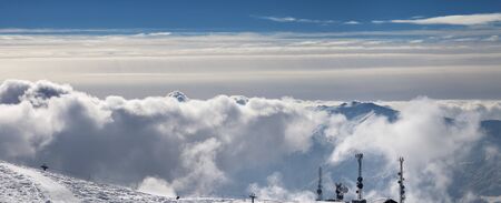 Panoramic view on snowy ski slope, satellite dishes and sun cloudy mountains. Caucasus Mountains in...