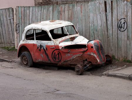 Broken vintage car on dirty roadside near old wooden fenceの写真素材