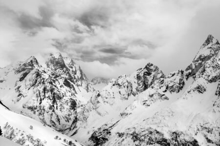 Gray high mountain peaks covered with ice and clouds at winter. Caucasus Mountains, region Dombay. Black and white toned landscape.の写真素材