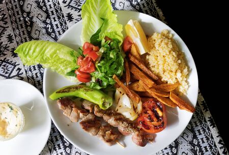 Traditional Turkish lunch. Grilled lamb kebab on wooden skewers with side dish and slice of lemon on table with tablecloth. View from above.の写真素材