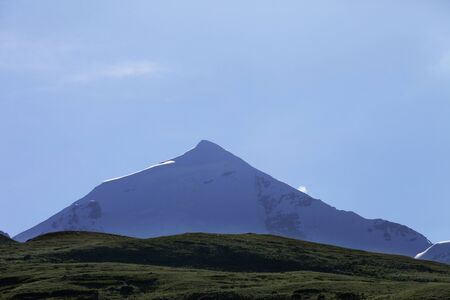 Silhouette of sunlit high snowy mountains with glacier, rocks and blue sky at early morning. Caucasus Mountains. Georgia, region Svanetia, Mount Tetnuldi.の写真素材